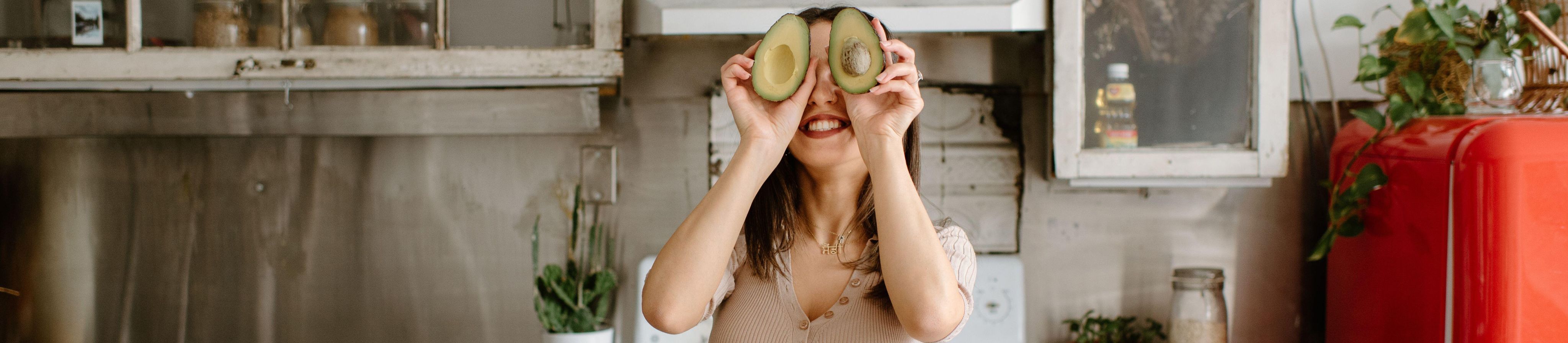 Smiling young woman holding avocado in front of face - Image ID: 2GG84G2 (RF)