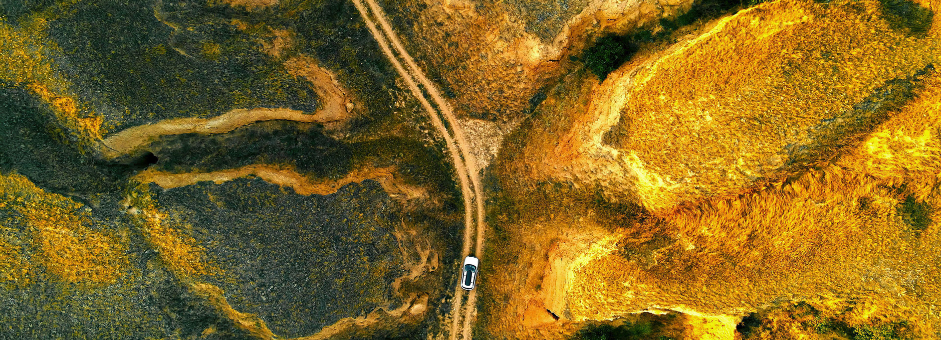 Aerial view of a car navigating through a rugged, winding dirt road amidst an arid landscape
