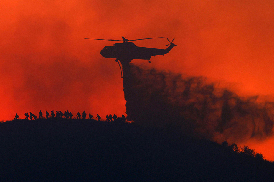 A water tanker drops water while firefighters walk below, as the Sandy Fire approaches  in Simi Valley