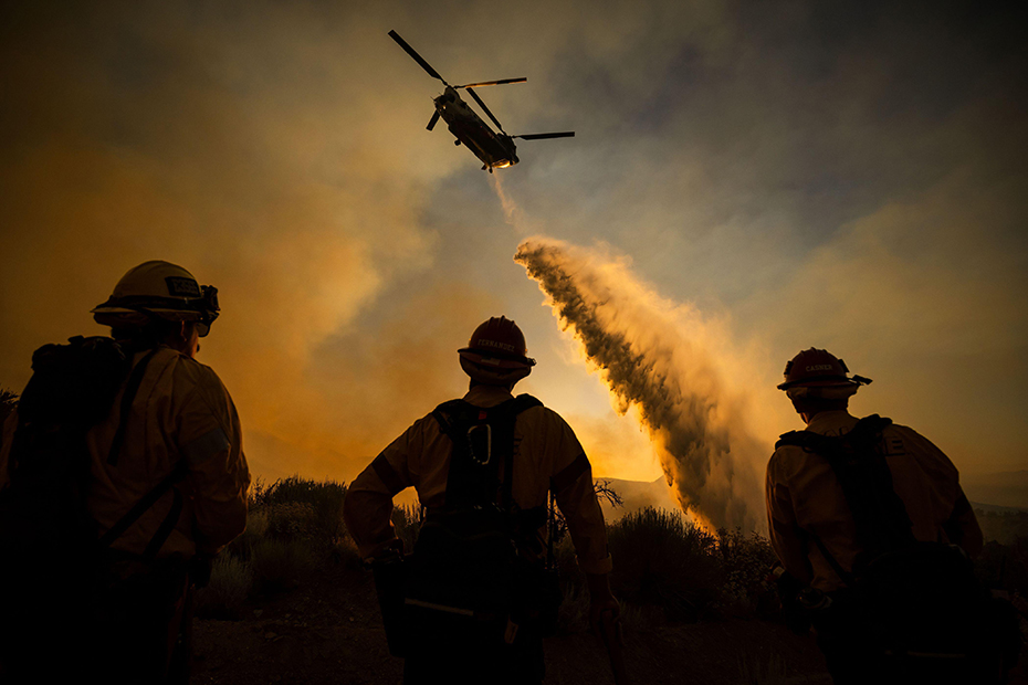 Firefighters watch as a helicopter drops water on the Summit Fire in Llano, CA.