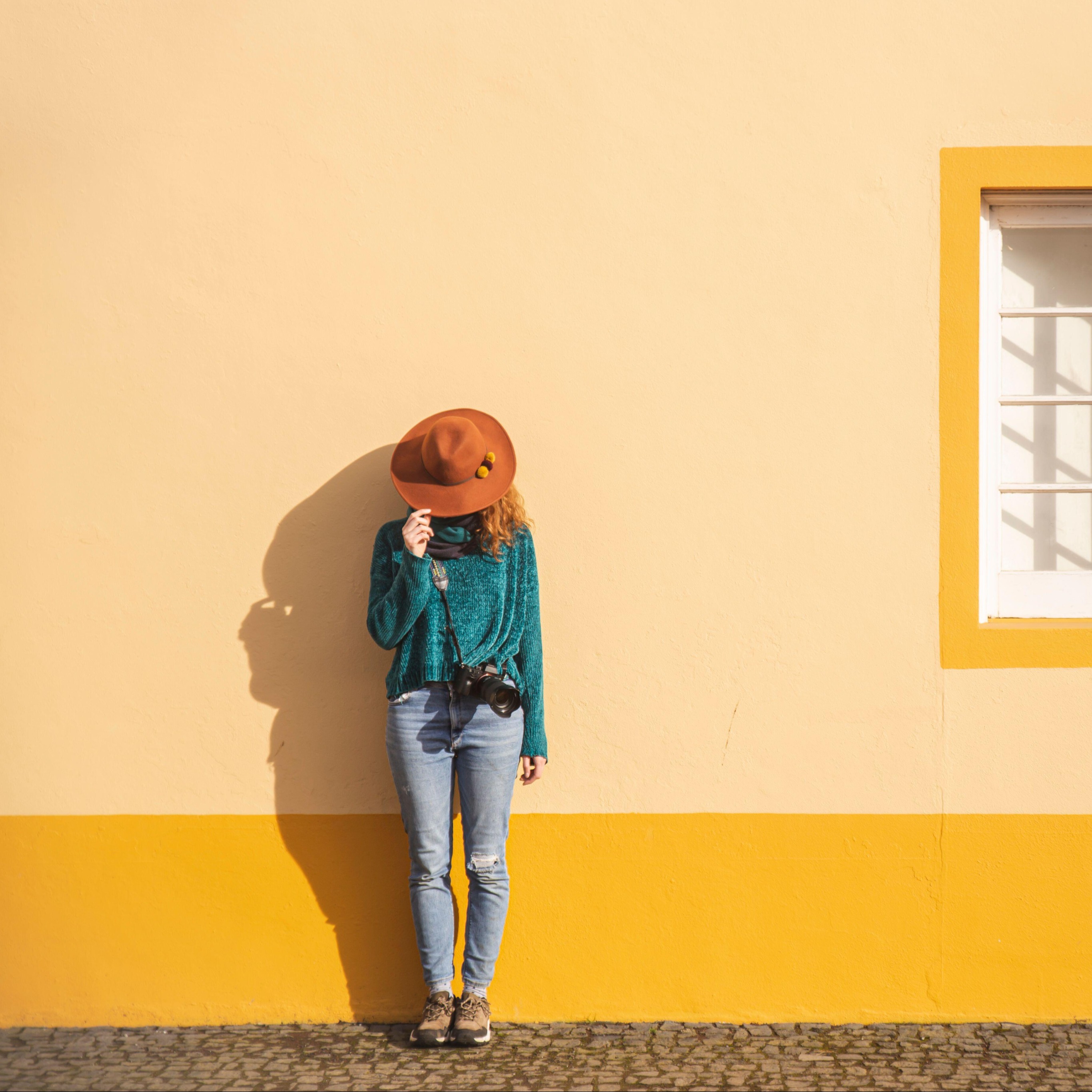 Woman with hat and camera standing in front of wall